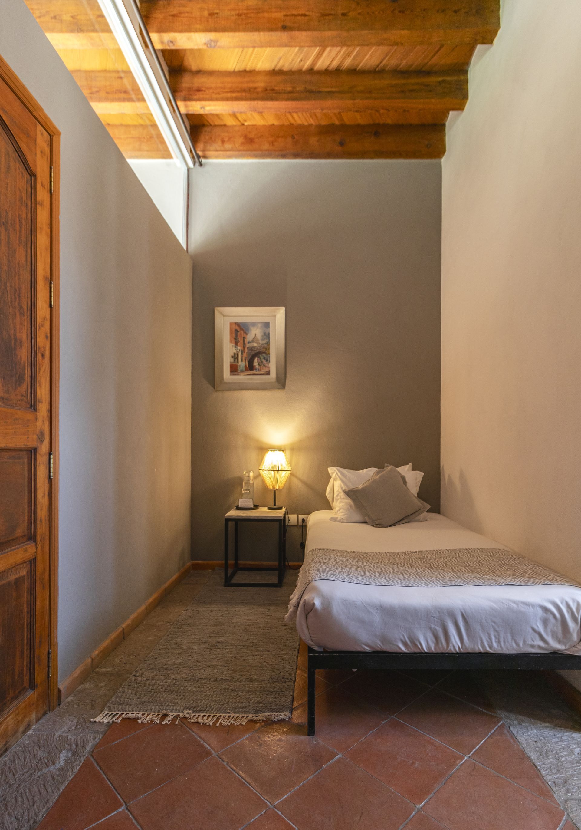 A small bedroom with a single bed and a wooden ceiling.