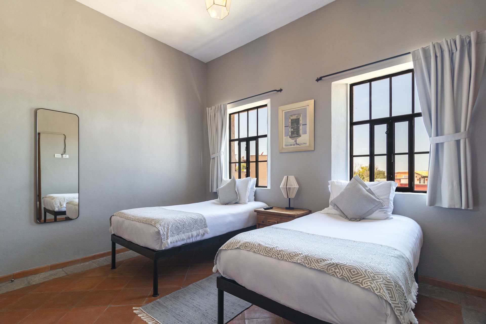 A bedroom with two beds , a mirror and two windows.