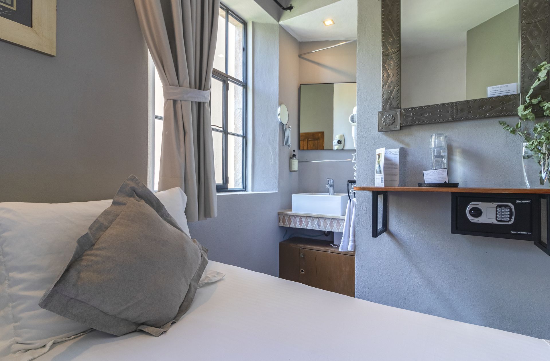 A hotel room with a bed , sink , mirror and safe.