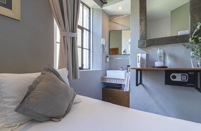 A hotel room with a bed , sink , mirror and safe.