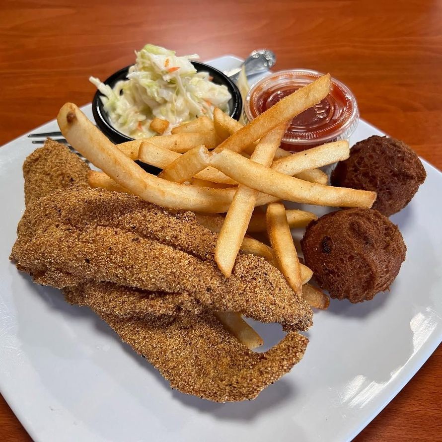 Fried fish plate with fries, coleslaw, hushpuppies, and ketchup on a white plate.