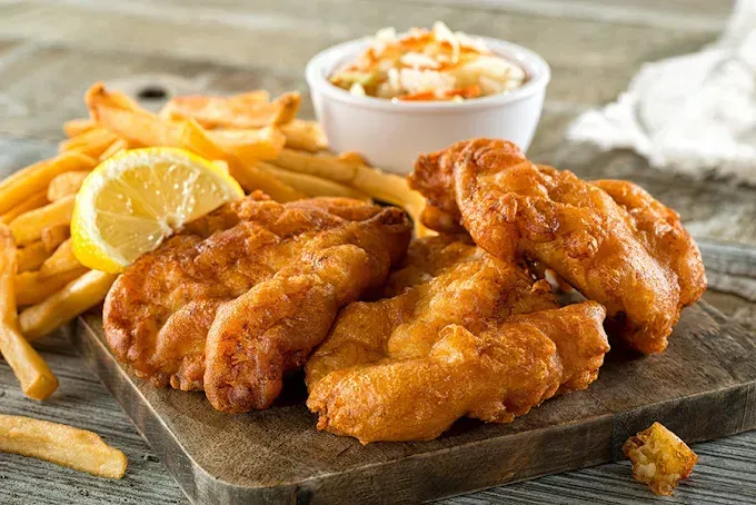 Fried fish fillets, fries, coleslaw, lemon on a wooden board.