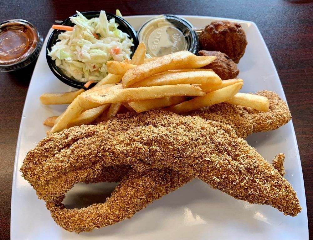 Fried catfish with fries, coleslaw, hushpuppies, and sauces on a white plate.