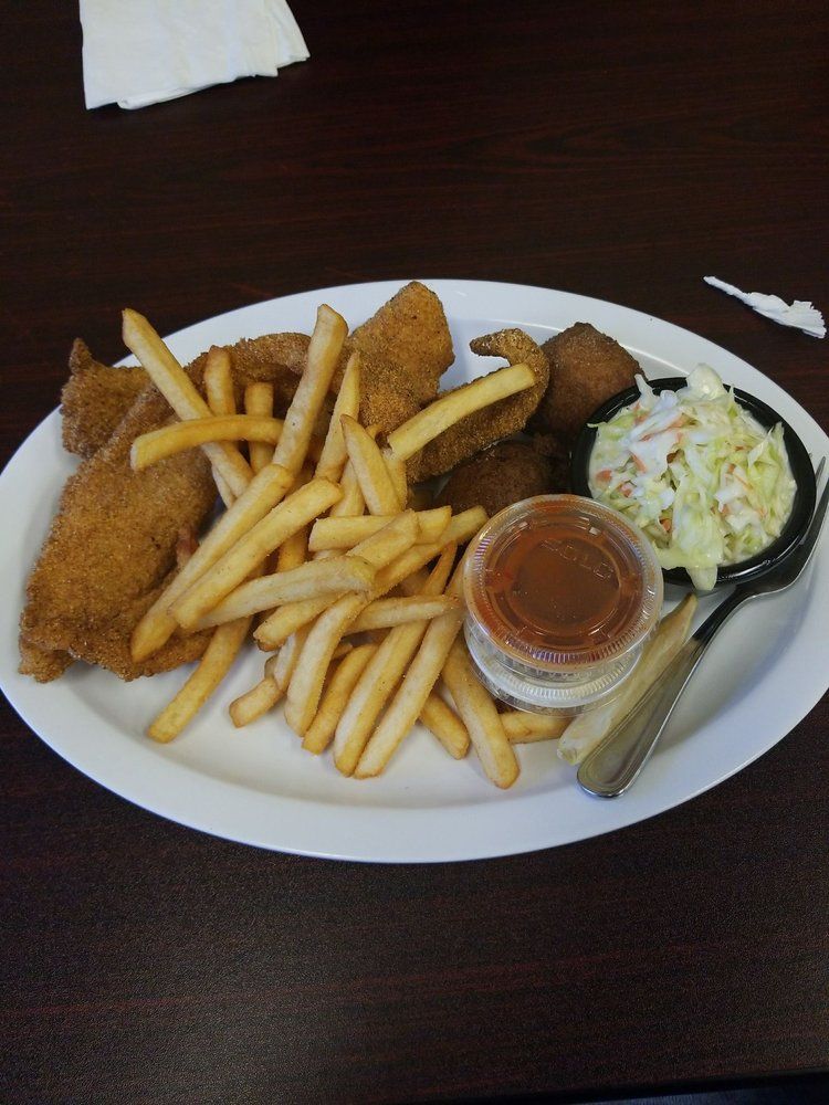 Plate of fried fish, fries, coleslaw, and sauce. White plate on a dark surface.
