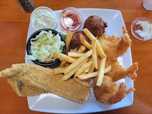 Plate of fried catfish, shrimp, fries, slaw, hushpuppy, sauces.
