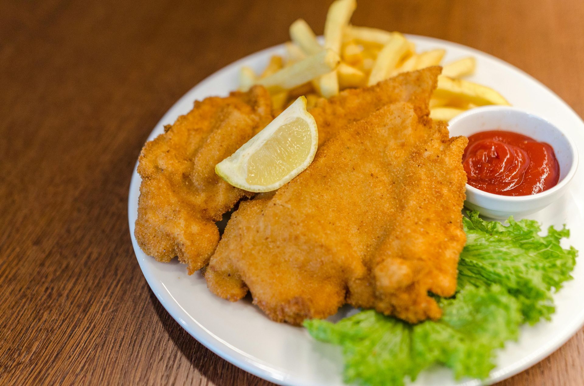 Breaded cutlets with fries, lemon wedge, ketchup, and lettuce on a white plate.