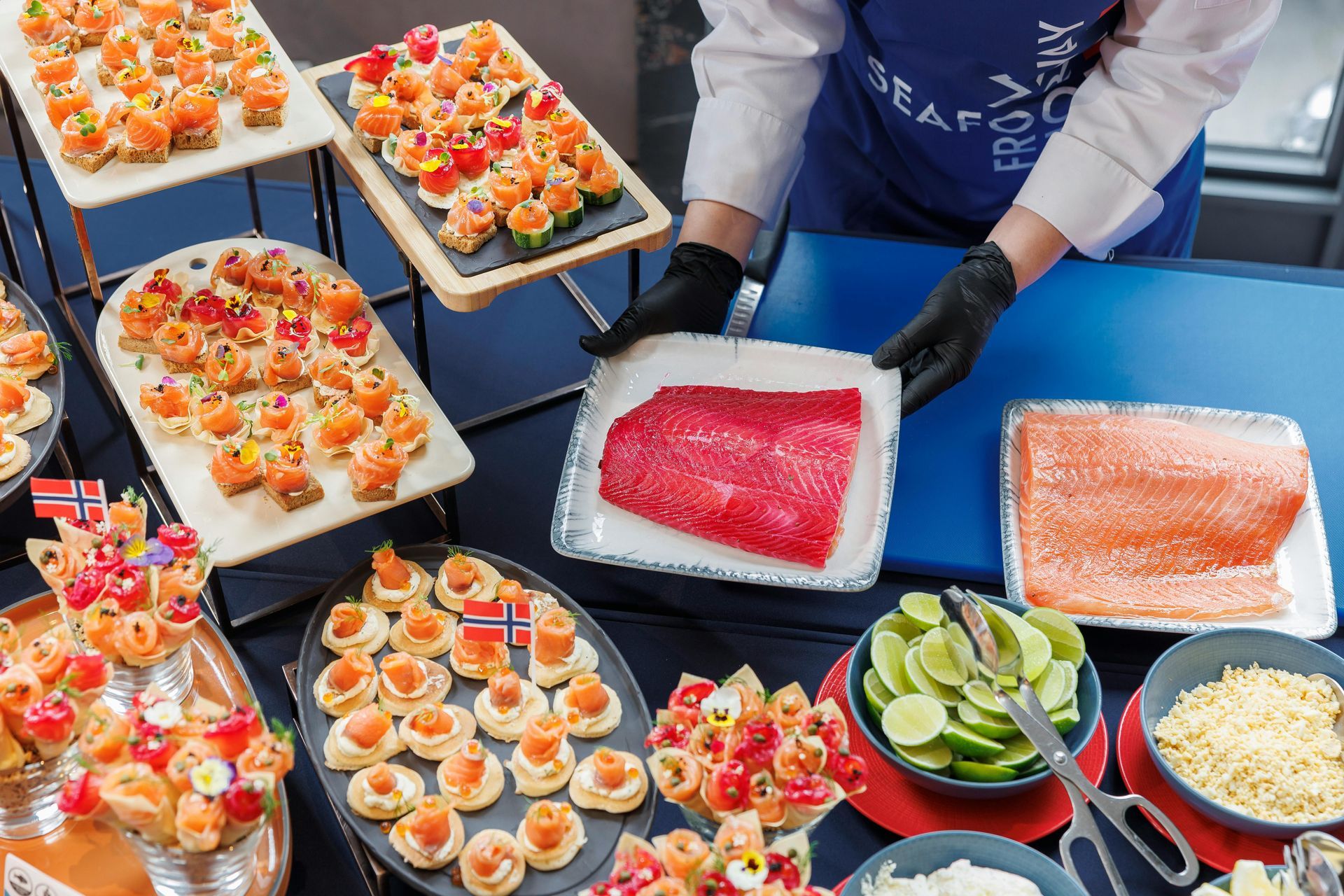 Person preparing salmon appetizers, displayed with ingredients and snacks.