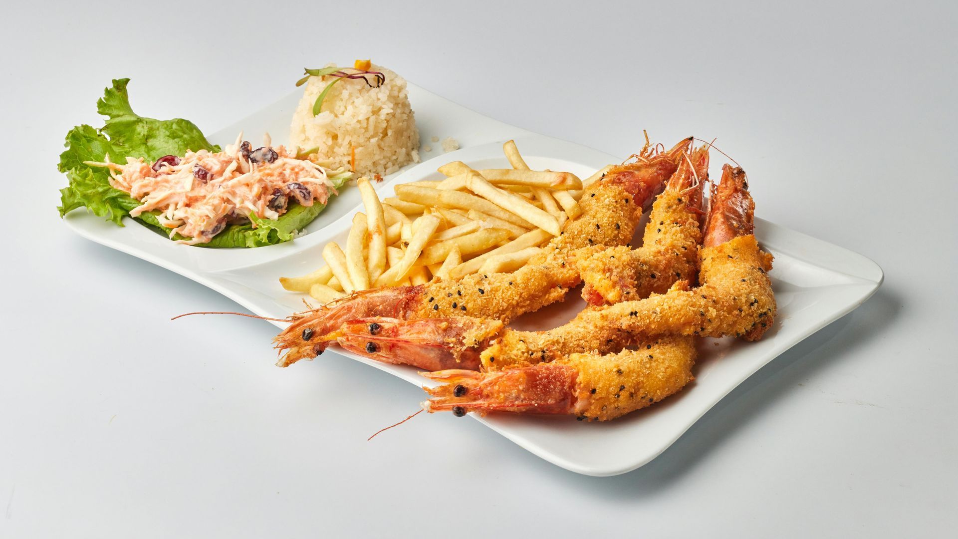 A white platter holding fried shrimp, french fries, a mound of rice, and a creamy salad with lettuce on a white background.