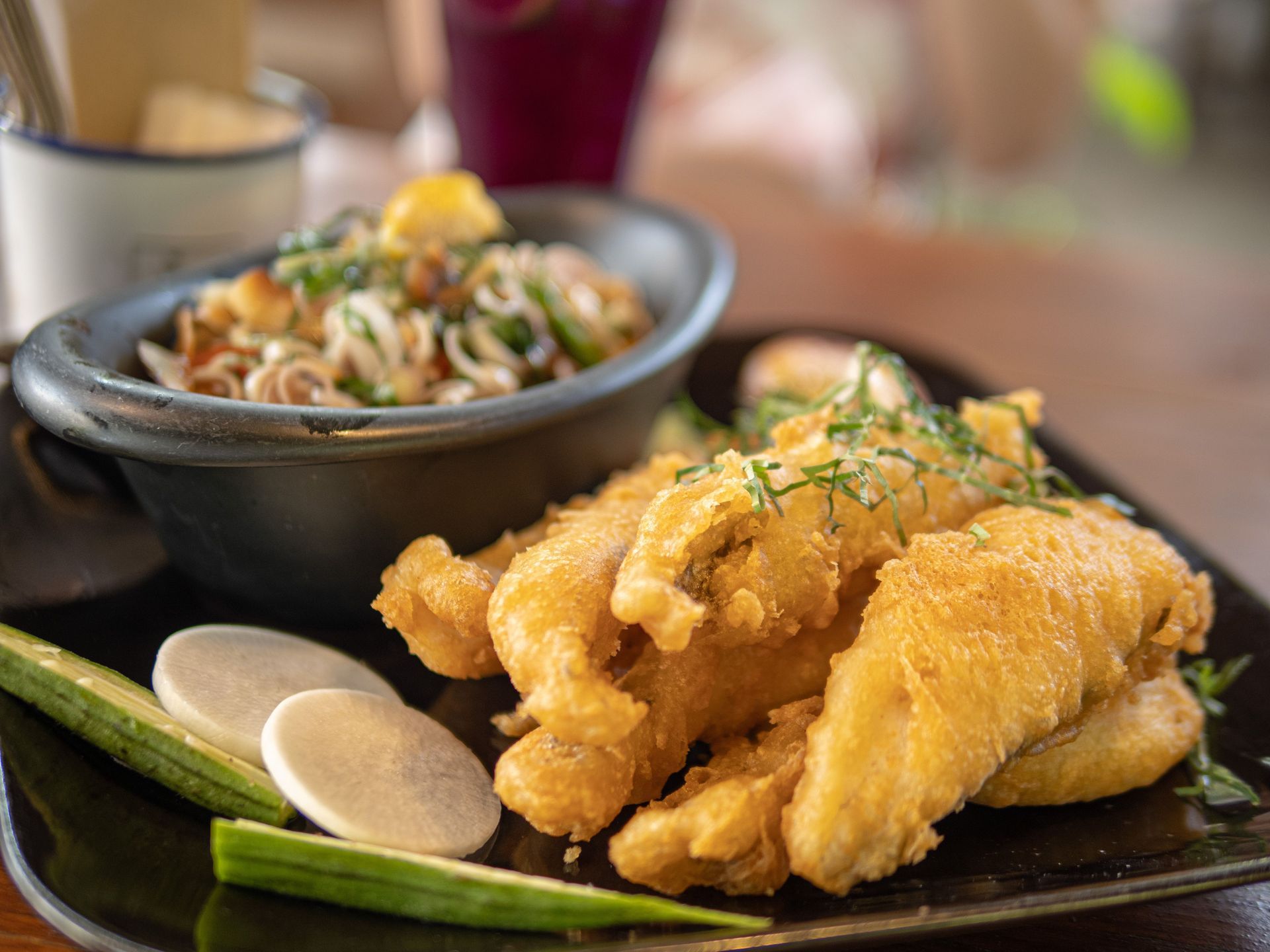 Golden fried fish with lemon wedges and a bowl of noodles on a table