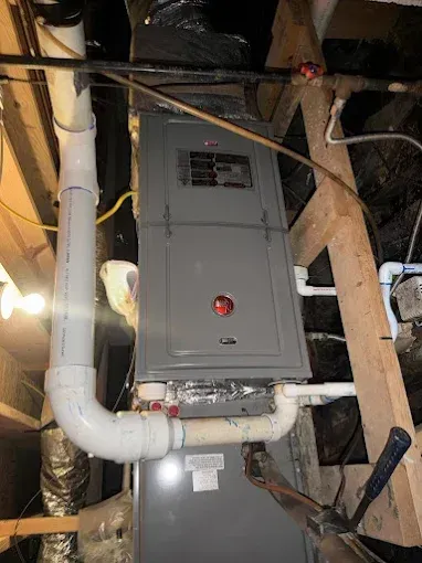 Gray furnace in a basement, with white pipes and wooden beams.