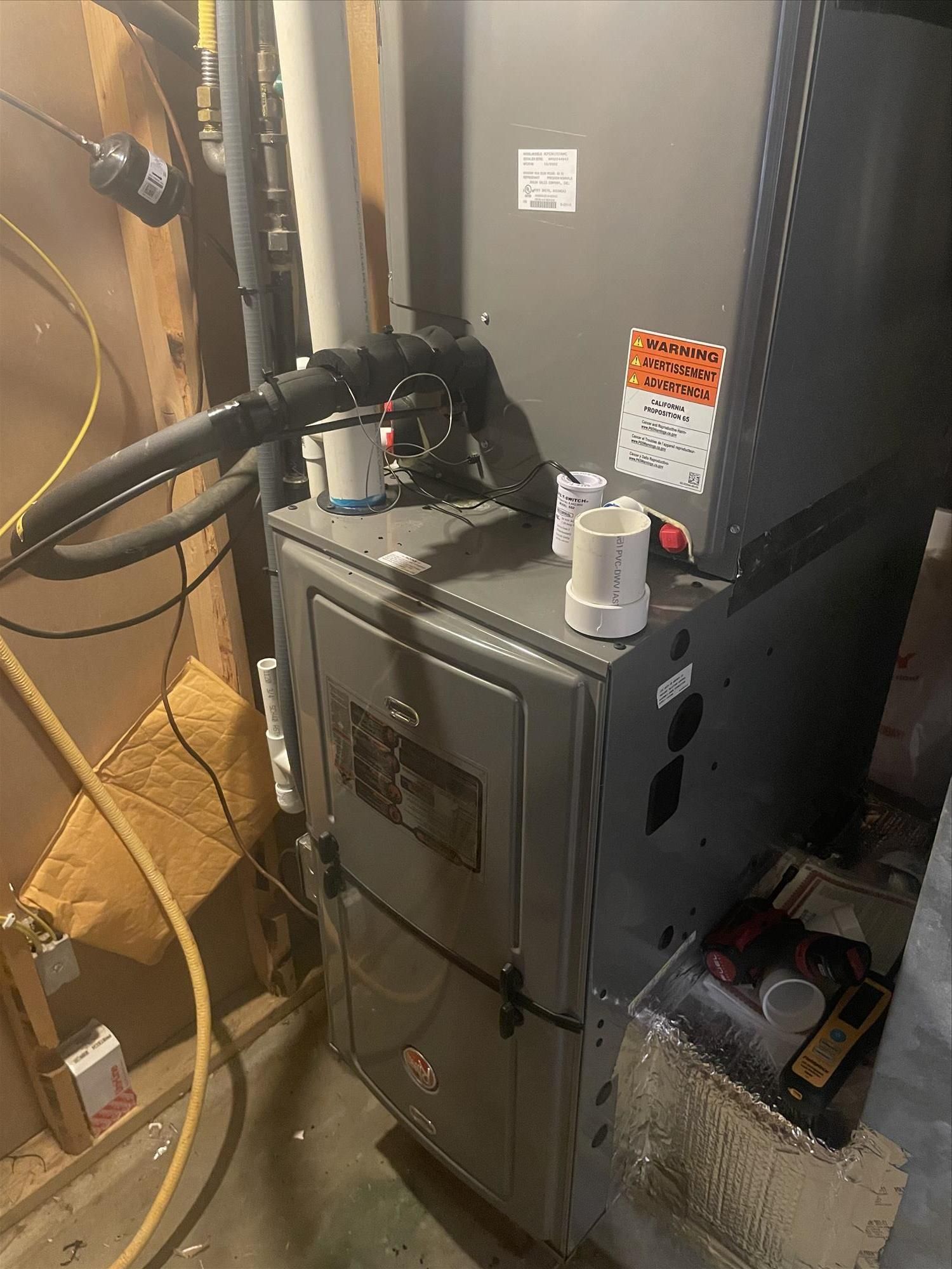 A gas furnace in a basement setting. Grey metal unit with pipes and venting.