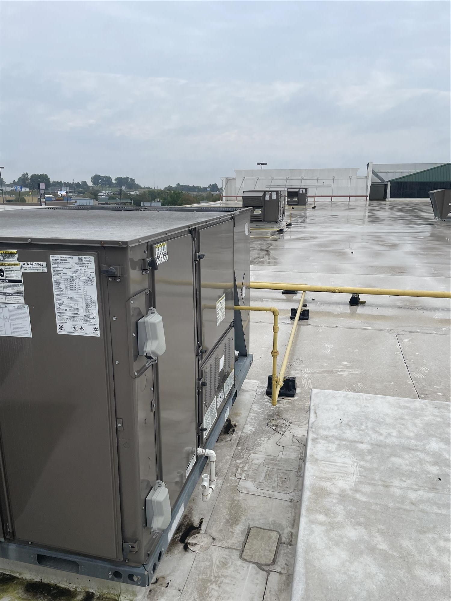 HVAC unit on a rooftop with a yellow safety railing, cloudy sky, and distant buildings.