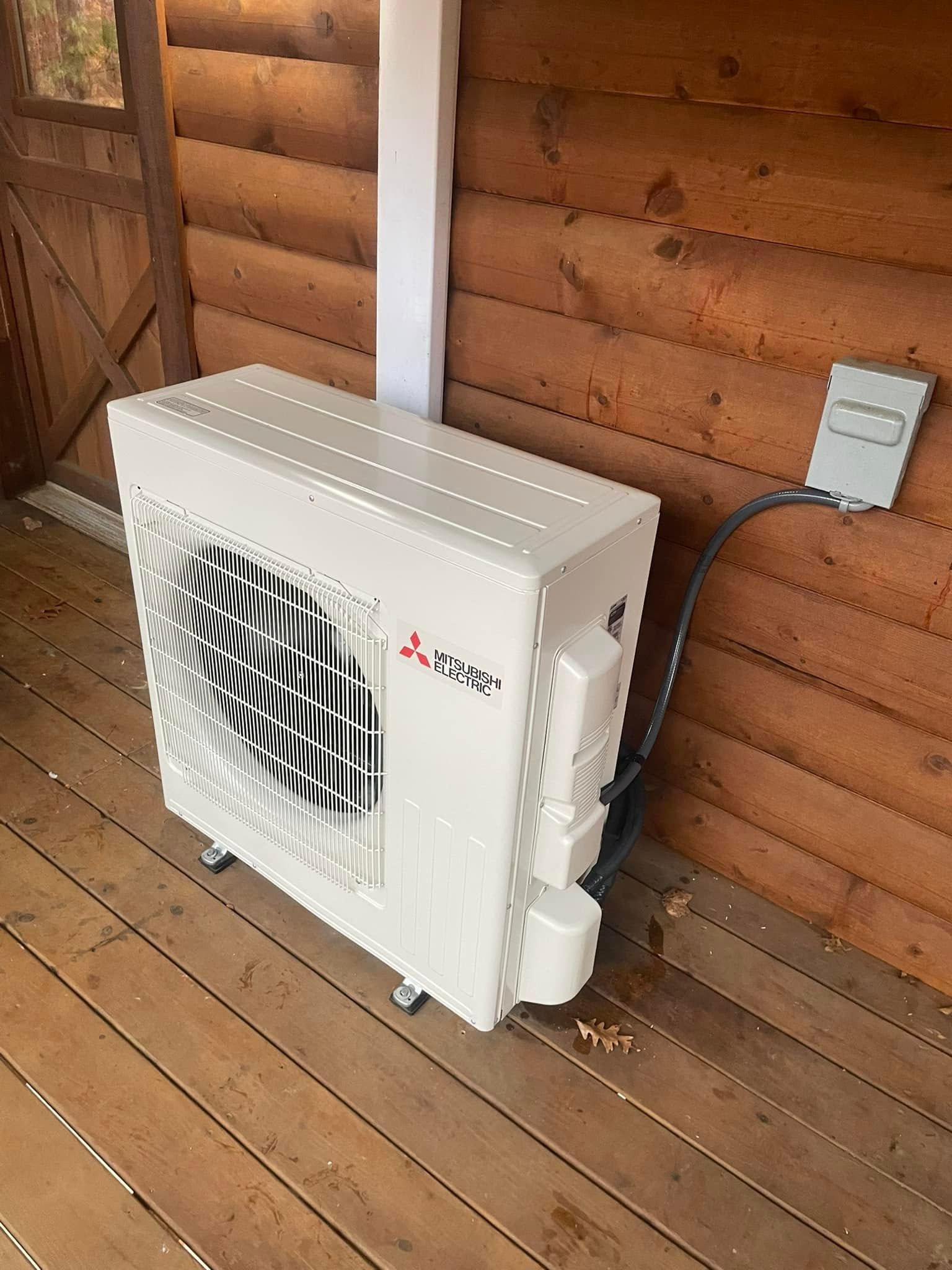 White Mitsubishi outdoor air conditioning unit on a wooden deck next to a wooden wall.