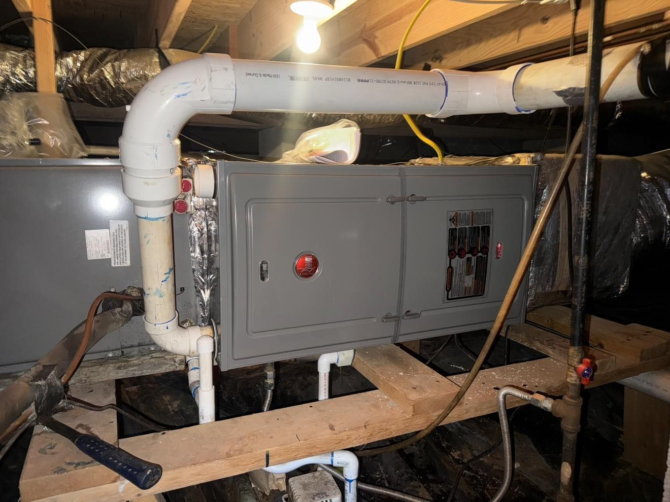 HVAC unit in crawl space with white PVC pipes and electrical components.