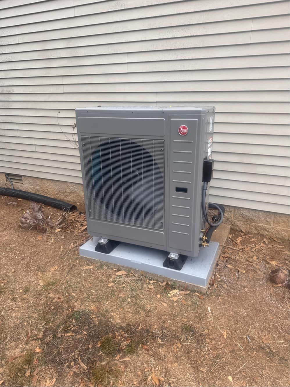 Grey heat pump unit on a concrete pad, beside a light-colored building, in a grassy yard.