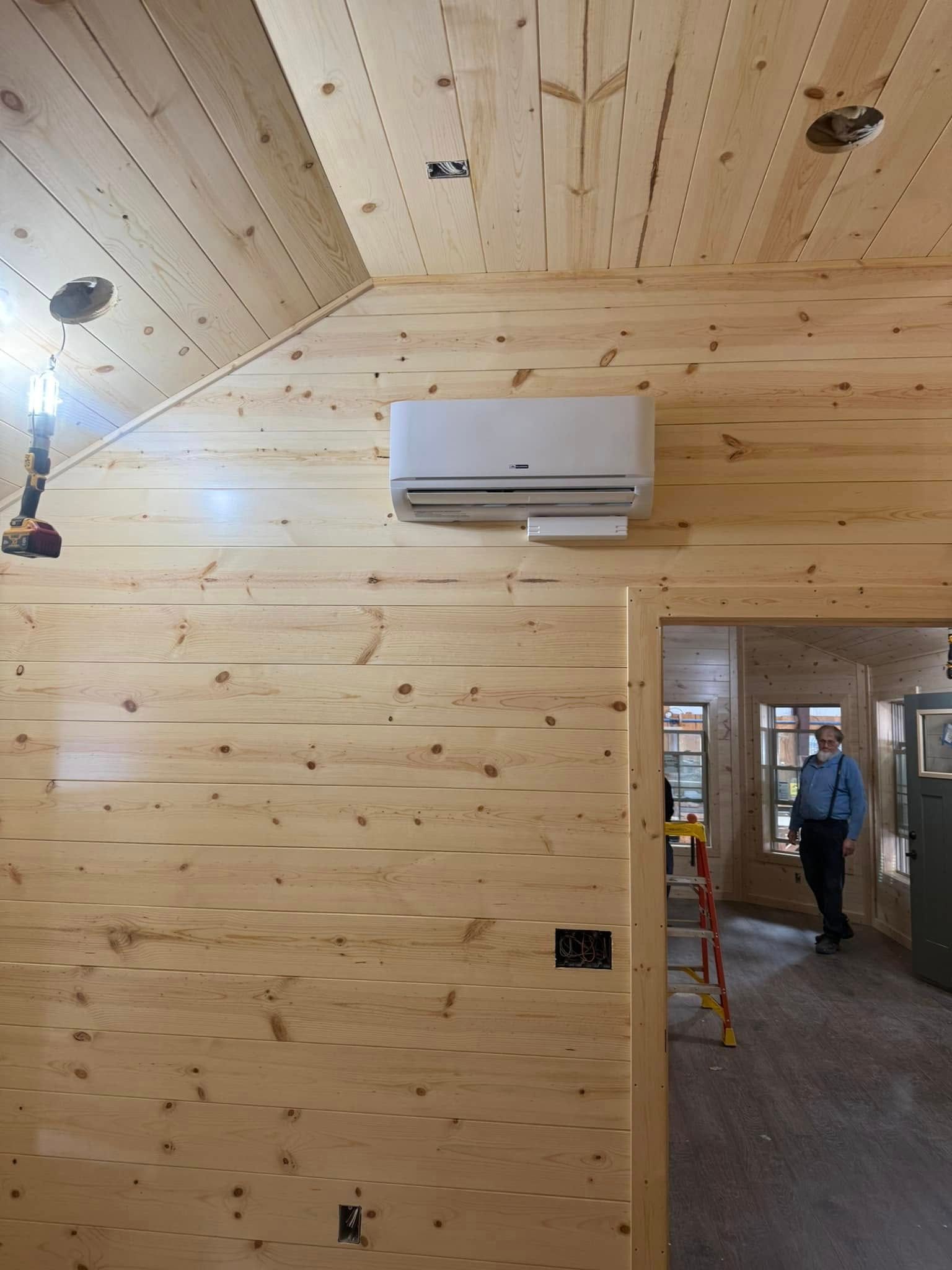 Interior view of wood-paneled room with a mounted air conditioner and a person standing in doorway.