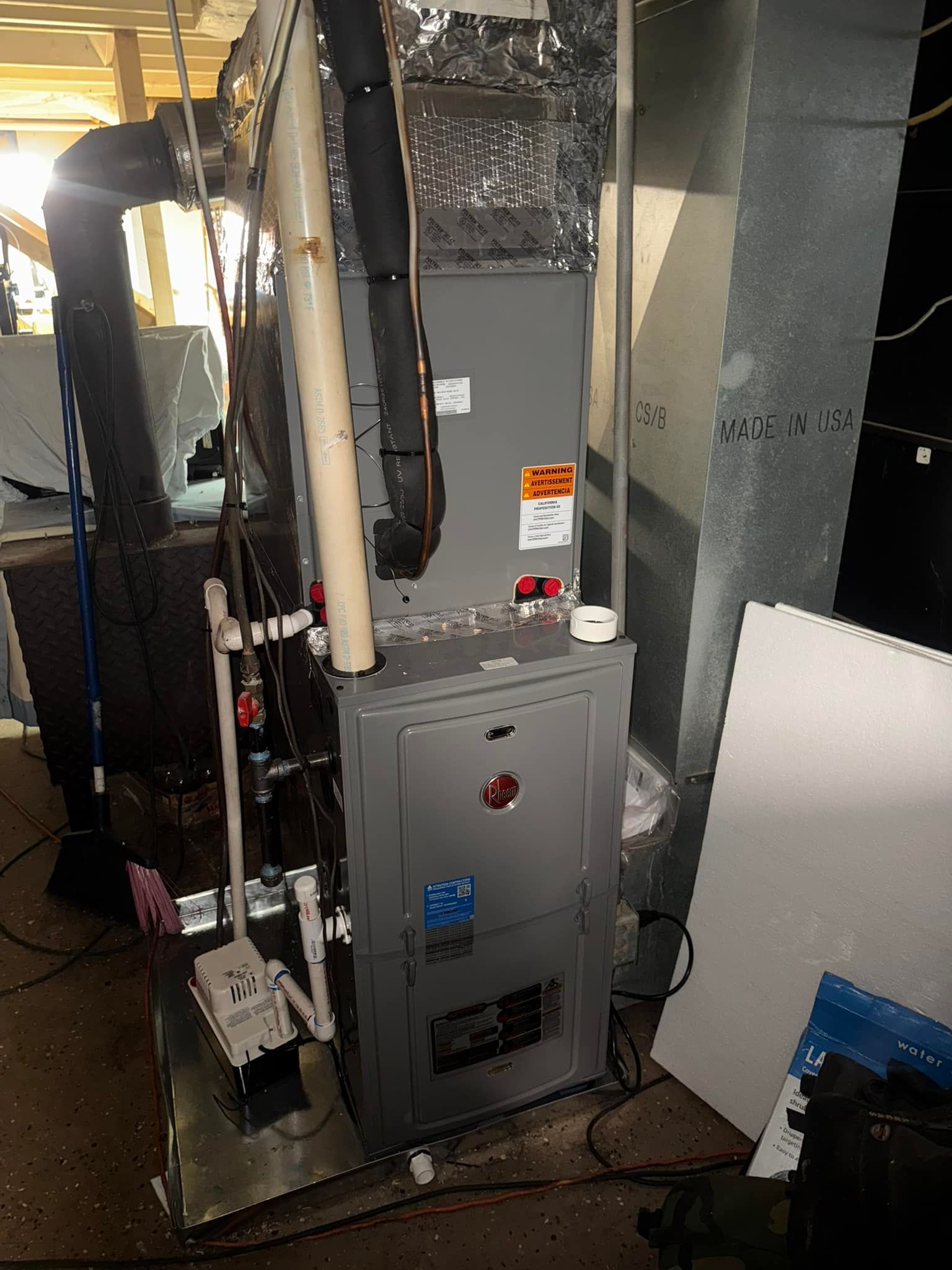 A gray HVAC unit in a basement setting with connected ductwork and pipes.