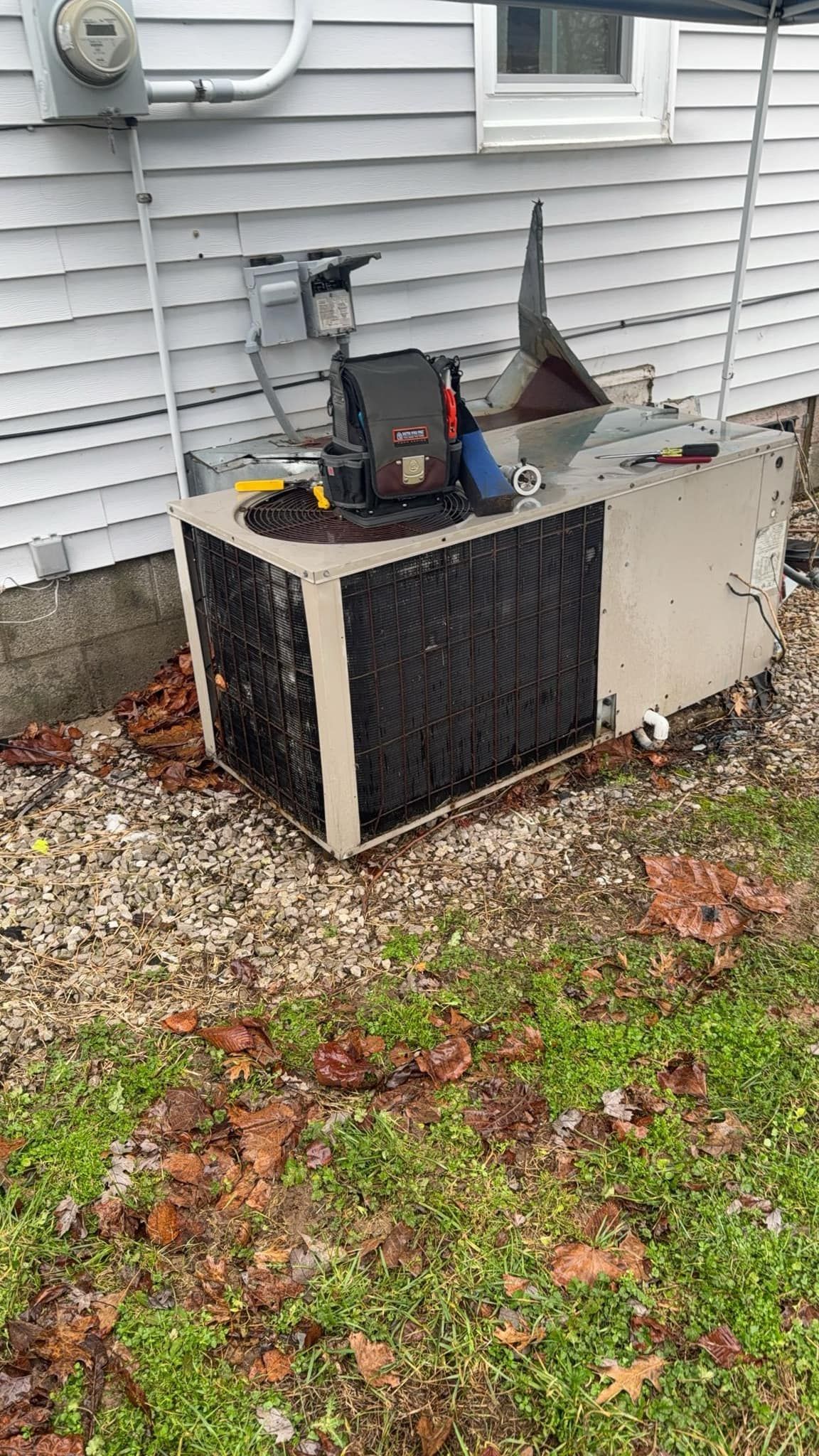 Exterior air conditioner unit next to a house, covered in debris and leaves.