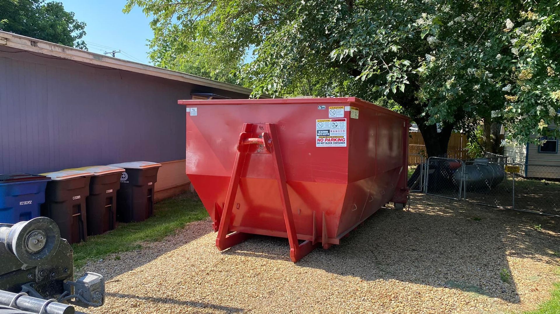 a red dumpster is parked in a gravel lot in front of a house .