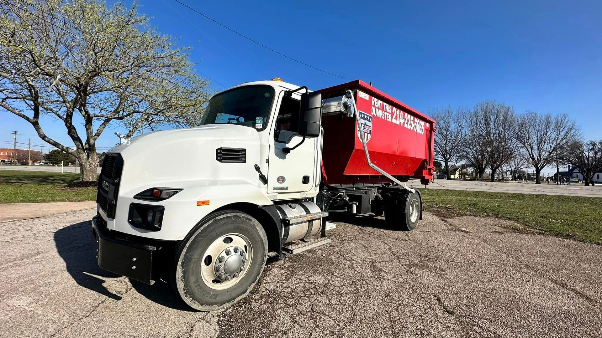 a white dump truck with a red dumpster attached to it is parked in a gravel lot .