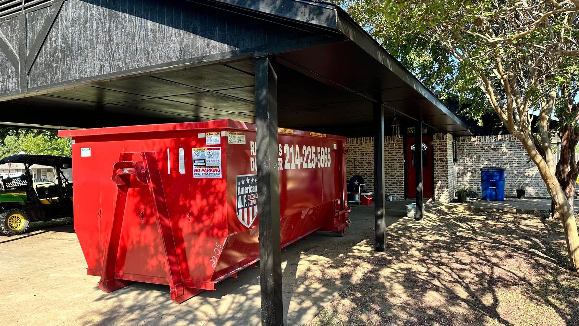 a red dumpster is parked under a canopy in front of a house .
