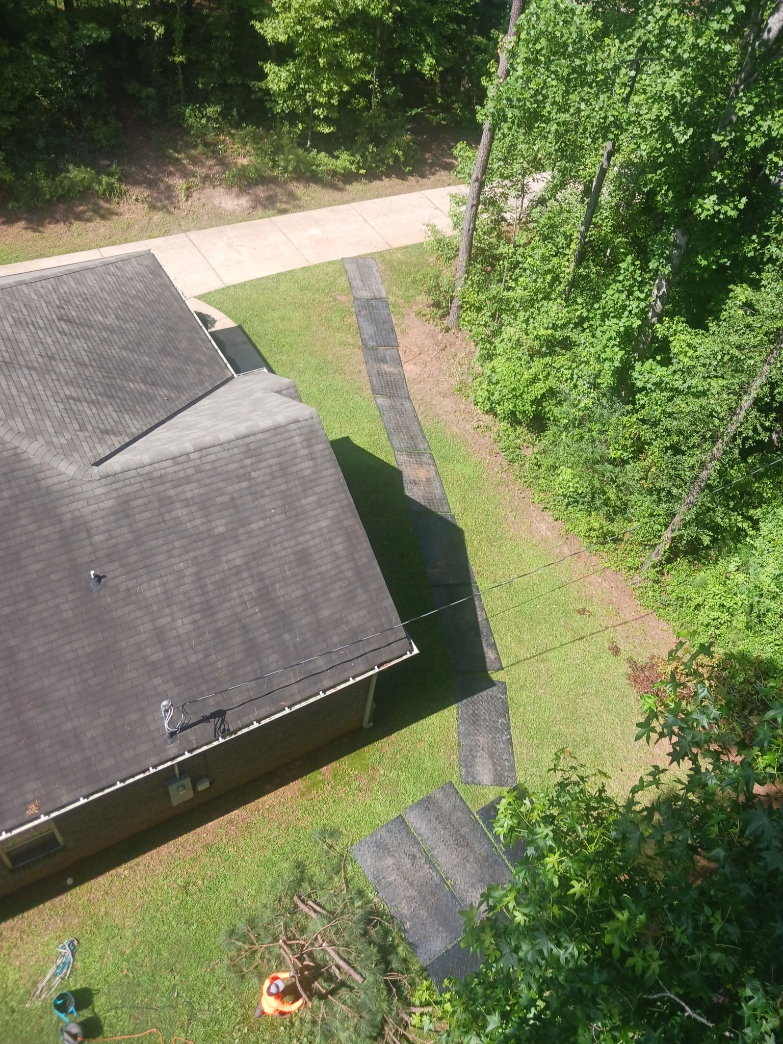 Overhead view of a house with a dark roof and surrounding green lawn and trees, and a concrete pathway.