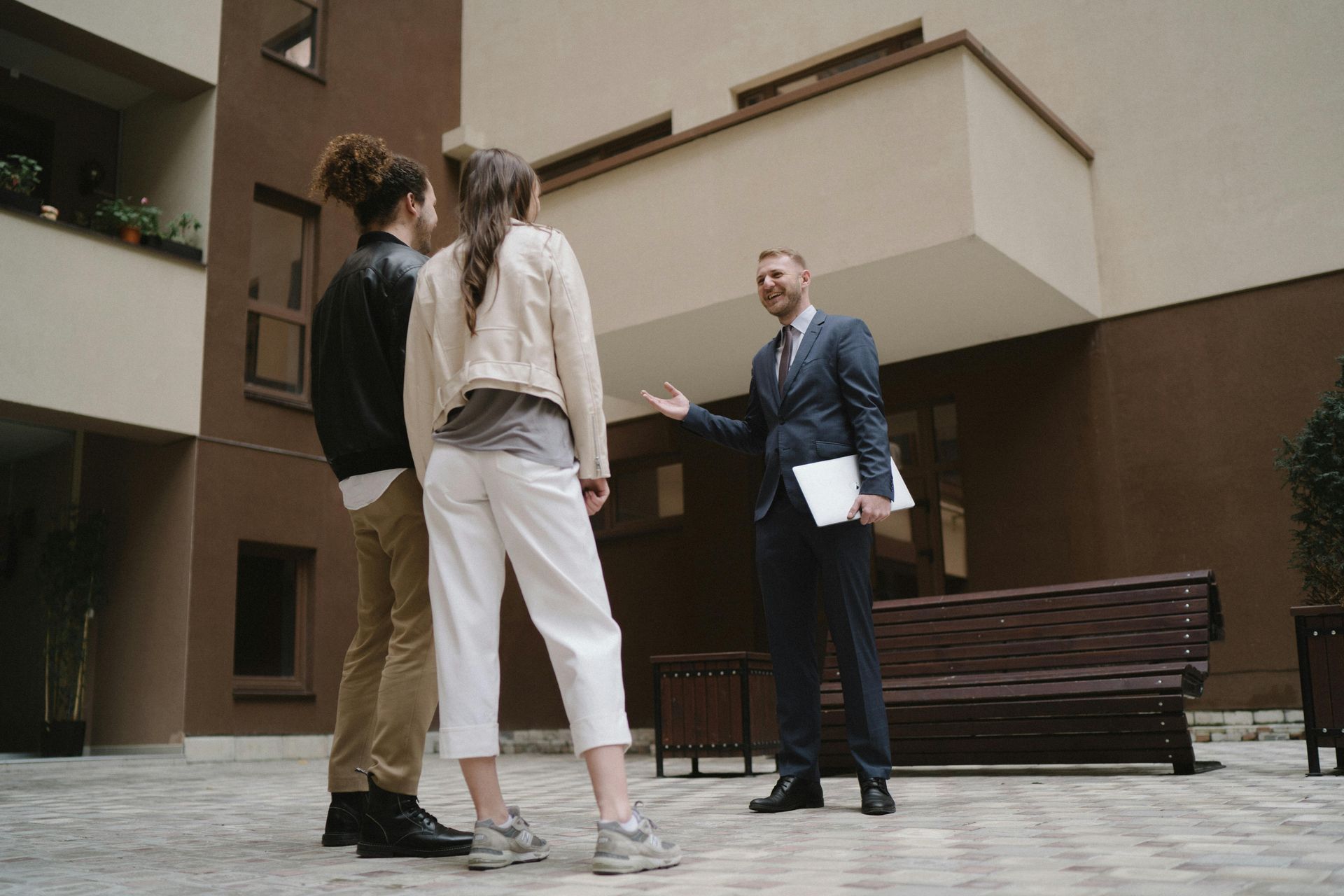 A man in a suit is talking to two people in front of a building