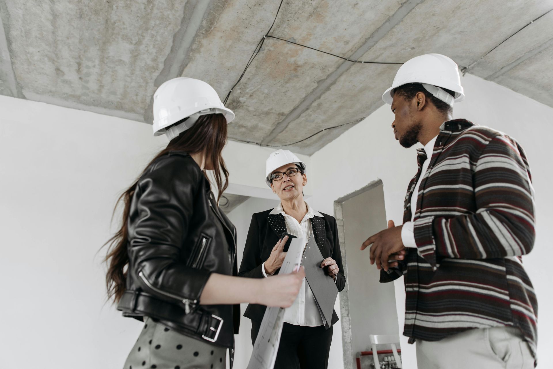 A group of people wearing hard hats are standing in a room talking to each other.