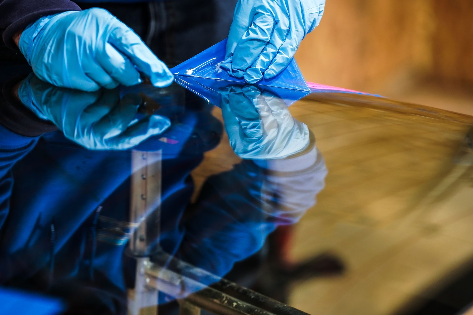 A person wearing blue gloves is working on a windshield.