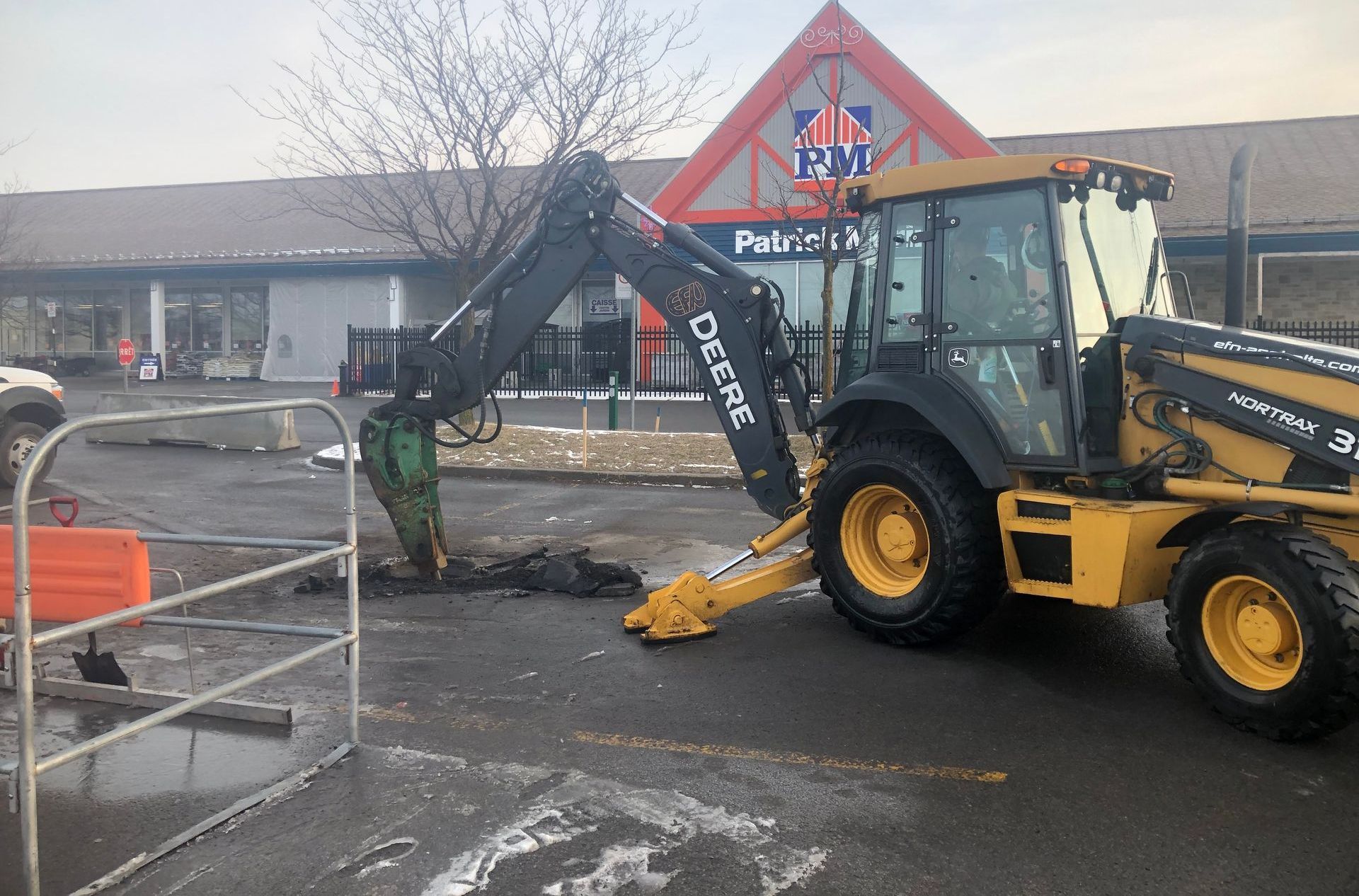 Un tracteur Yellow Deere creuse un trou dans un parking