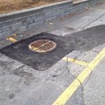 Une plaque d'égout est posée sur le bord de la route à côté d'une ligne jaune.