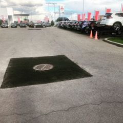 Une rangée de voitures est garée dans un parking à côté d'une plaque d'égout.