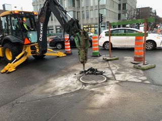 Une excavatrice Deere travaille sur une plaque d'égout dans une rue de la ville.