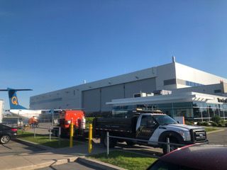 Un camion est garé devant un grand bâtiment avec un avion en arrière-plan.