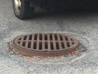 Une plaque d'égout est posée sur le sol à côté d'une voiture.