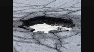 Une photo en noir et blanc d'un nid-de-poule sur la route.