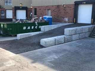 Une benne à ordures verte se trouve devant un bâtiment à côté d'une rampe.