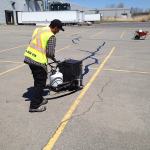 Un homme en gilet jaune trace une ligne sur un parking.