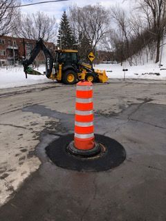 Un tracteur jaune circule dans une rue à côté d'un cône orange.