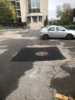 Une voiture blanche est garée dans un parking à côté d'une plaque d'égout.