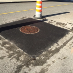 Une plaque d'égout se trouve sur le bord de la route, à côté d'un cône de signalisation.