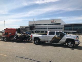 Un camion blanc auquel est attachée une remorque est garé devant un grand bâtiment.