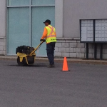 Un homme pousse une brouette dans un parking à côté d'un cône orange.