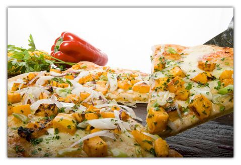 Porción de pizza con ingredientes, servida en un plato de madera, apoyada sobre una espátula de plata.