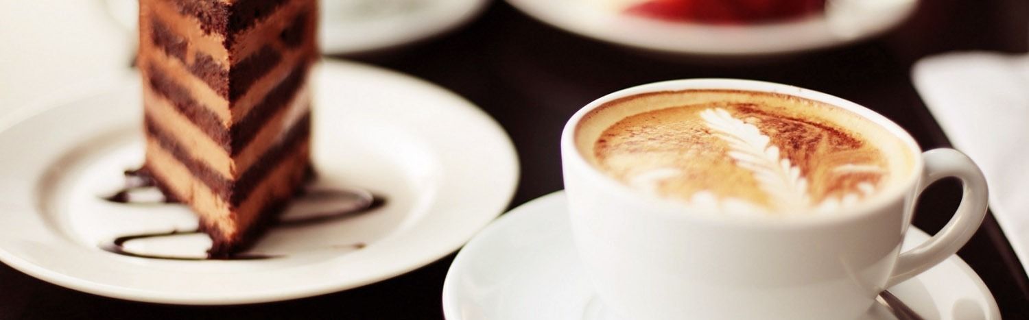 Rebanada de pastel de chocolate en un plato blanco con una taza de café.