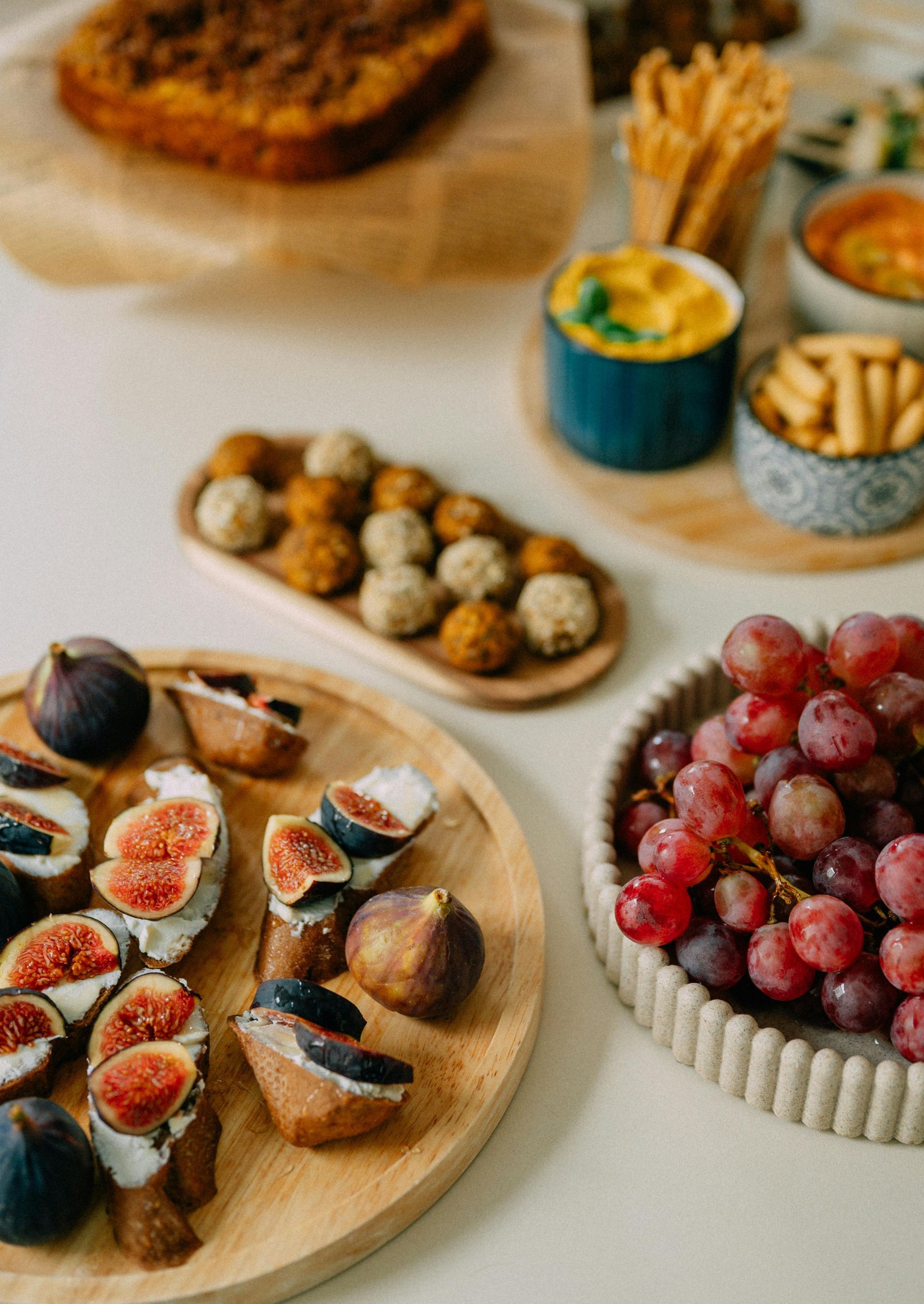 Una mesa repleta de aperitivos, entre ellos higos con queso, albóndigas, uvas y salsas.