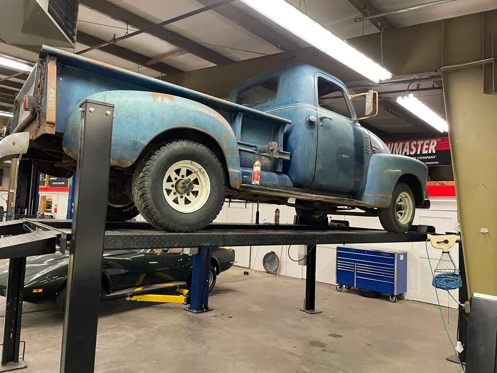 Blue vintage pickup truck on a car lift in a workshop.