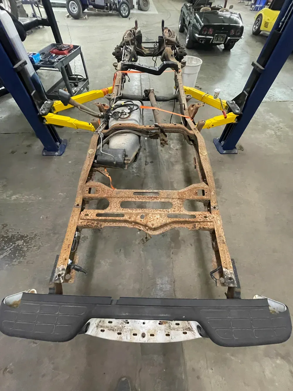 Rusting truck frame on a lift in a garage.