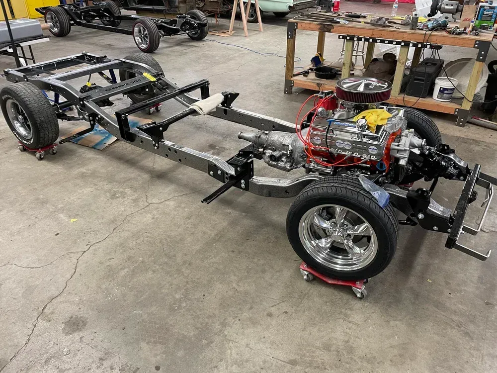 Car chassis with engine and wheels, in a garage.