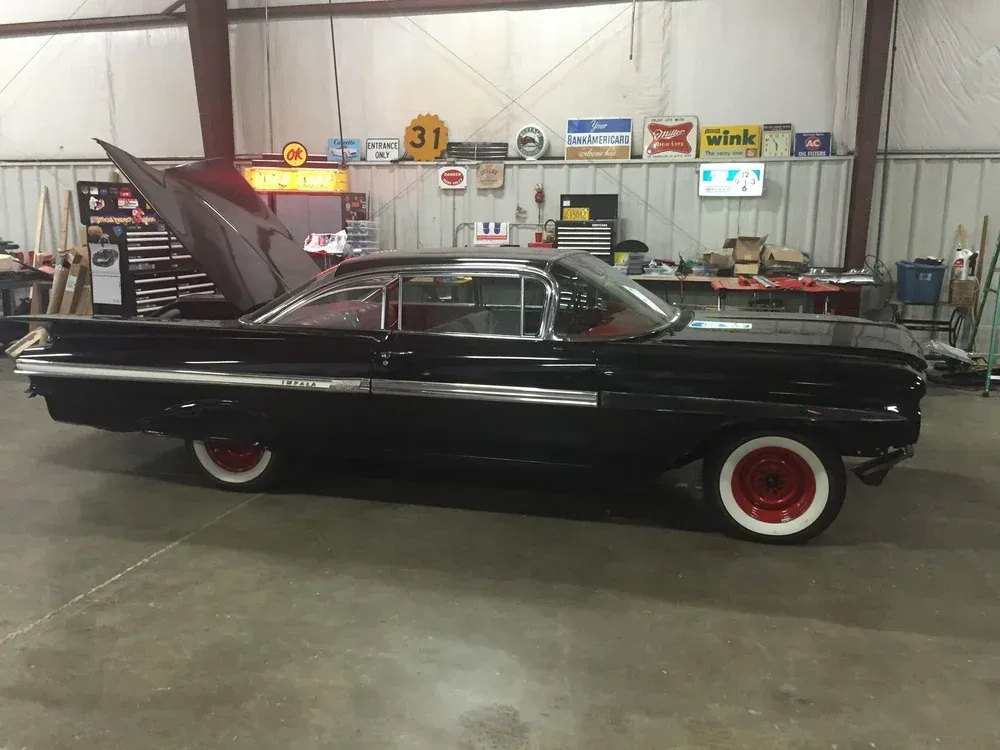 Black classic car with fins and red wheels inside a garage.